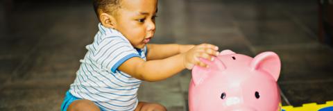 Child Tax Credit Toddler putting money into pink piggy bank.