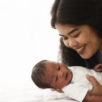 Mixed race African American and Asian mother holding her newborn baby with happy face.