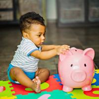 Toddler putting money into pink piggy bank.