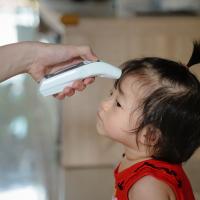 Toddler getting her temperature taken by child care provider.