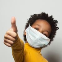 Thumbs up from a masked young child. 