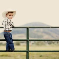 Young child on a fence with cowboy hat.