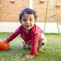 Toddler plays with a ball outside and smiles for the camera.