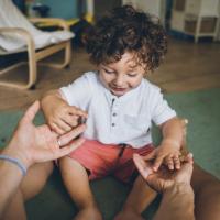 Toddler taking his teacher's hands.