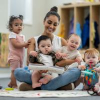 Child care provider reading to a diverse group of babies on her lap. 