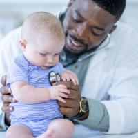 African American male doctor listening to a white baby's heart. 