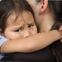 A little girl with sad eyes hugging her mom. 