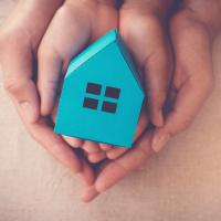 Parent and child hands holding a small cardboard blue house.