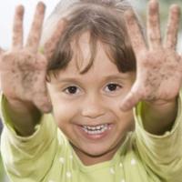 Beautiful little girl having fun outdoors and showing her dirty hands 