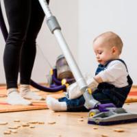 Woman cleaning with vacuum cleaner, baby sitting on floor and biscuits all around 