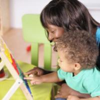 Close-up view of biracial baby/toddler and African-American woman using abacus to learn through play. 