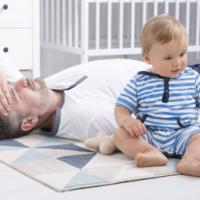 cropped shot of a tired father lying on the floor next to his little baby 