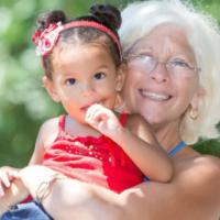 caucasian grandmother carrying her small latin granddaughter 