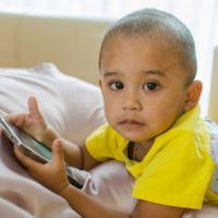 Preschool boy plays with smart phone on the bed. 