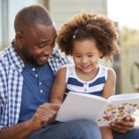 Young black father and daughter reading book outside 