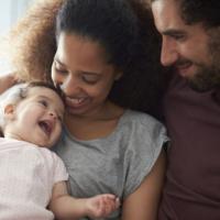 Parents Sitting On Sofa Cuddling Baby Daughter At Home 