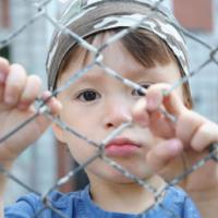 caucasian boy looking sadly through the bars outdoor 