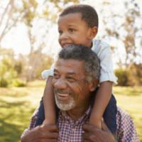 Grandfather Carries Grandson On Shoulders During Walk In Park 