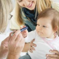 Mother holding her cute baby girl while pediatrician doing an eyesight test with diagnostic light pen. Selective focus to cute baby. 