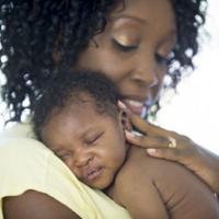 A mother is holding her newborn baby in her arms. They child is sleeping against her shoulder. 