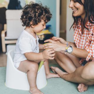 Mom helping her toddler son to learn how to use the potty. 