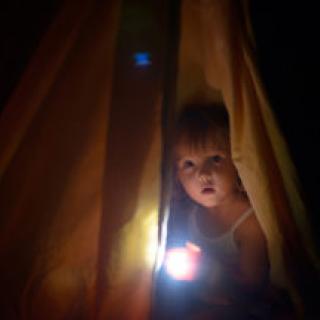 The girl under a cover holds at dark night a small lamp in hand 
