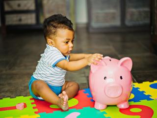 Toddler putting money into pink piggy bank.