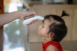 Toddler getting her temperature taken by child care provider.