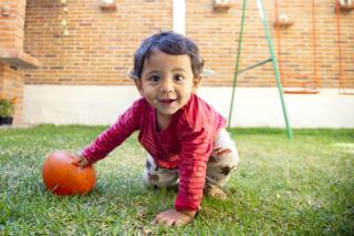 Toddler plays with a ball outside and smiles for the camera.