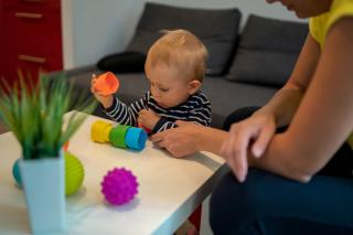 No the odds baby. Baby looking at plastic blocks on a table.