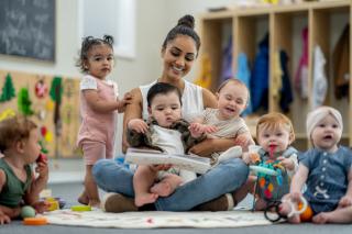 Child care provider reading to a diverse group of babies on her lap. 