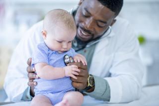 Public vs Private African American male doctor listening to a white baby's heart.