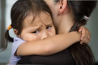 A little girl with sad eyes hugging her mom. 