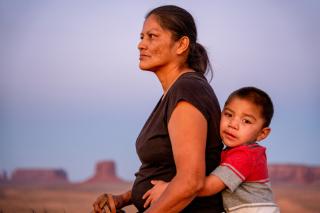 Navajo Mother and Young Four Year Old Son posing horseback in front of the Buttes in the Monument Valley Tribal Park in Northern Arizona at Sunset.