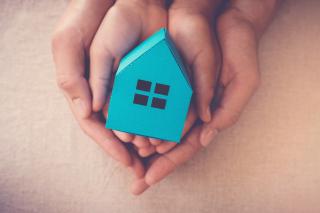 Housing Disruptions Parent and child hands holding a small cardboard blue house.