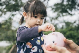 MD Families Spending Upwards of 32% of Income on Child Care Little girl putting coins in a piggy bank.