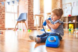 LOCATE 2024 Beautiful toddler sitting on the floor playing with vintage phone at kindergarten.