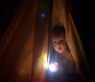 The girl under a cover holds at dark night a small lamp in hand 