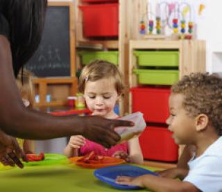 A portrait of a biracial toddler showing excitement at the prosprct of receiving more food at nursery.