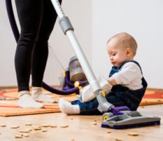 Woman cleaning with vacuum cleaner, baby sitting on floor and biscuits all around 