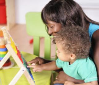 Close-up view of biracial baby/toddler and African-American woman using abacus to learn through play. 