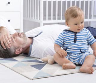 cropped shot of a tired father lying on the floor next to his little baby