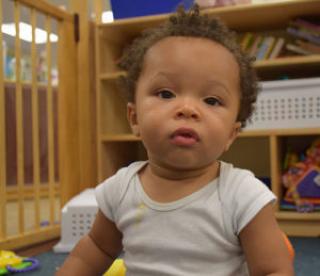 Toddler boy in onesie looks straight at camera