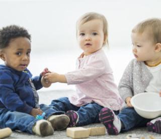 A multi-ethnic group of babies are playing with toys together at daycare.