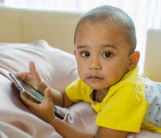 Preschool boy plays with smart phone on the bed. 