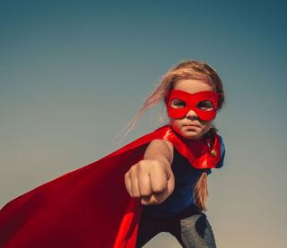 Funny little power super hero child (girl) in a red raincoat. Superhero concept.