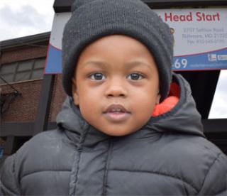 Smiling little boy bundled up in from of Early Head Start center 