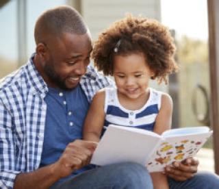 Young black father and daughter reading book outside