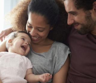 Parents Sitting On Sofa Cuddling Baby Daughter At Home
