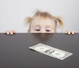 portrait of blonde caucasian baby nineteen month age with pigtails chubby face yellow shirt looking at dollar banknote on brown table 